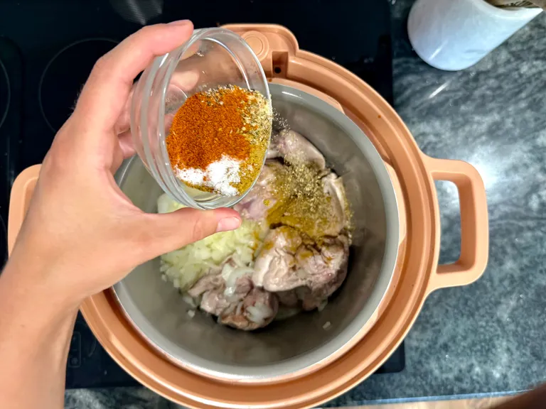 Seasoning chicken thighs and onions in a pressure cooker for chicken enchilada bake