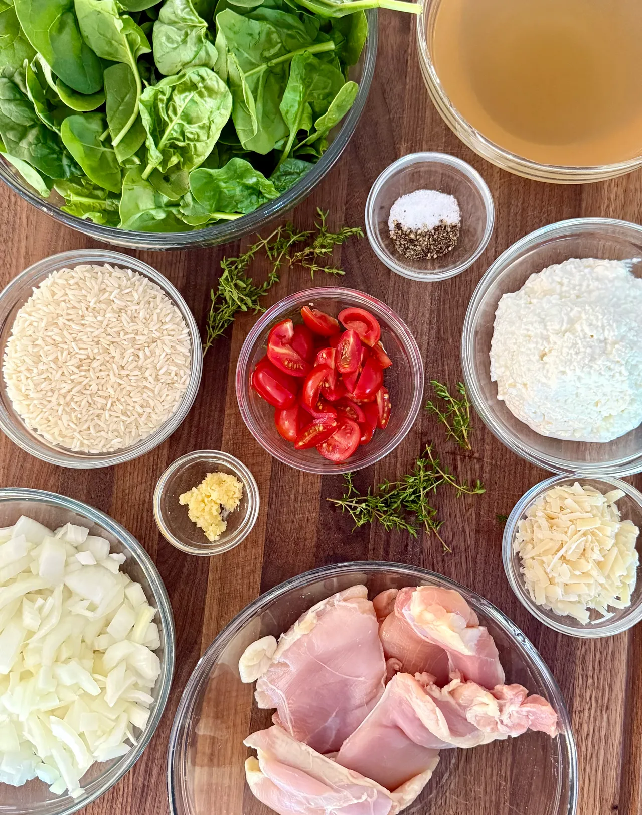 Ingredients for a high-protein chicken, rice, spinach, and cottage cheese casserole arranged on a wooden cutting board, including chicken, rice, fresh spinach, tomatoes, Parmesan cheese, onion, garlic, and chicken broth.