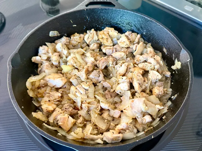 Chicken thighs and onions browning in a cast iron skillet with garlic and herbs while preparing a high-protein chicken, rice, spinach, and cottage cheese casserole for meal prep and freezer meals.