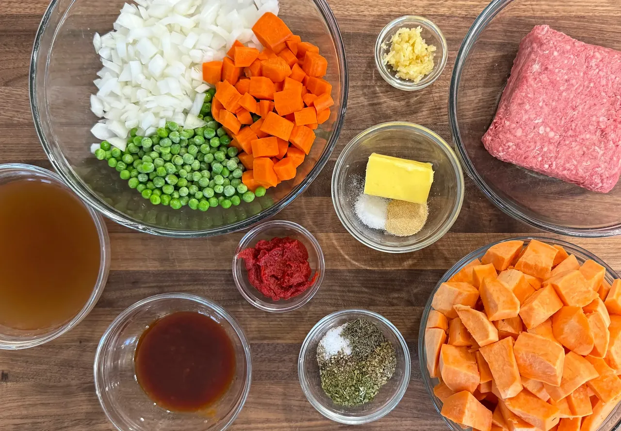 Ingredients for sweet potato cottage pie including ground beef, sweet potatoes, carrots, peas, onions, garlic, beef broth, tomato paste, and herbs for postpartum freezer meal prep and healthy family dinners.