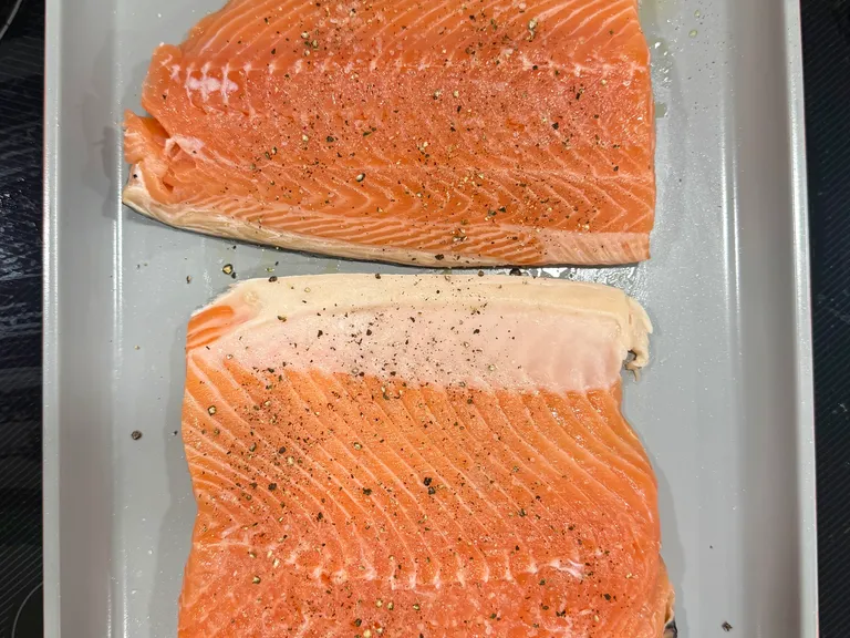 Fresh salmon fillets seasoned with salt and black pepper on a ceramic baking sheet before roasting for healthy salmon sweet potato cakes.