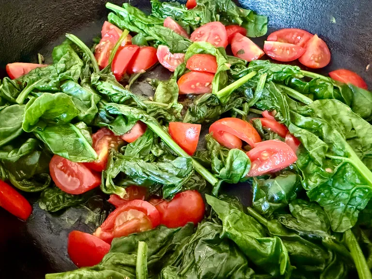 Fresh spinach and grape tomatoes sautéing in a cast iron skillet while preparing a high-protein chicken, rice, spinach, and cottage cheese casserole for meal prep and freezer meals.