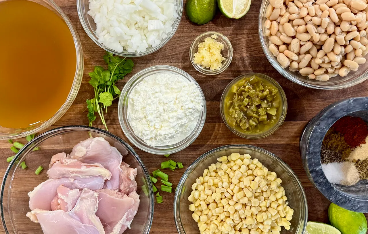 Ingredients for high-protein white chicken chili including chicken thighs, white beans, corn, cottage cheese, chicken broth, green chiles, garlic, onion, lime, and spices for meal prep and postpartum freezer meals.
