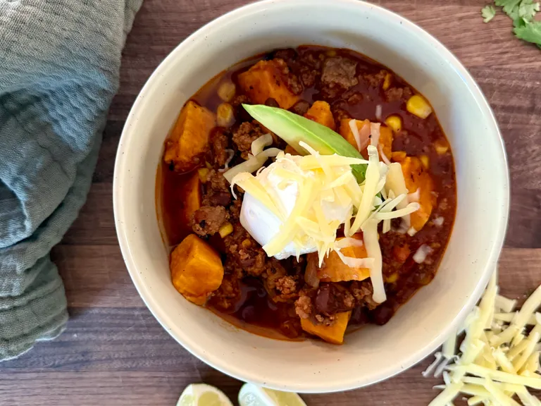 Healthy postpartum beef and sweet potato chili with black beans, corn, and lean ground beef topped with sour cream, cheddar cheese, and avocado