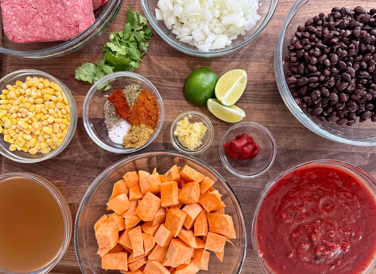 Ingredients for healthy beef and sweet potato chili including lean ground beef, sweet potatoes, black beans, corn, onions, garlic, tomatoes, broth, and chili seasonings.